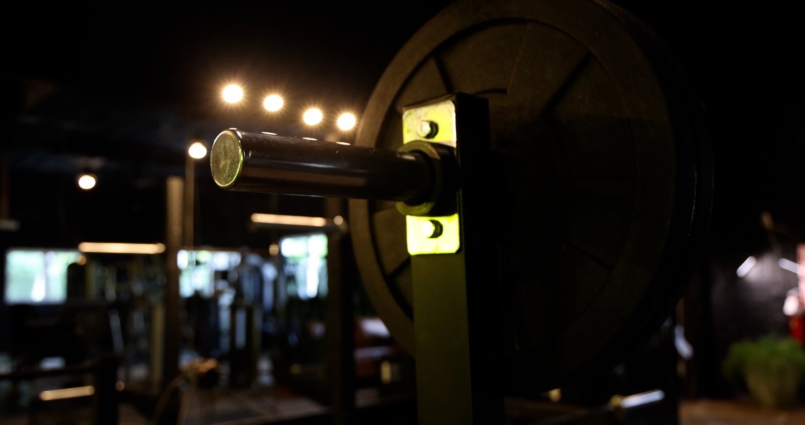 A loaded barbell racked in the half light, floor lights behind it
